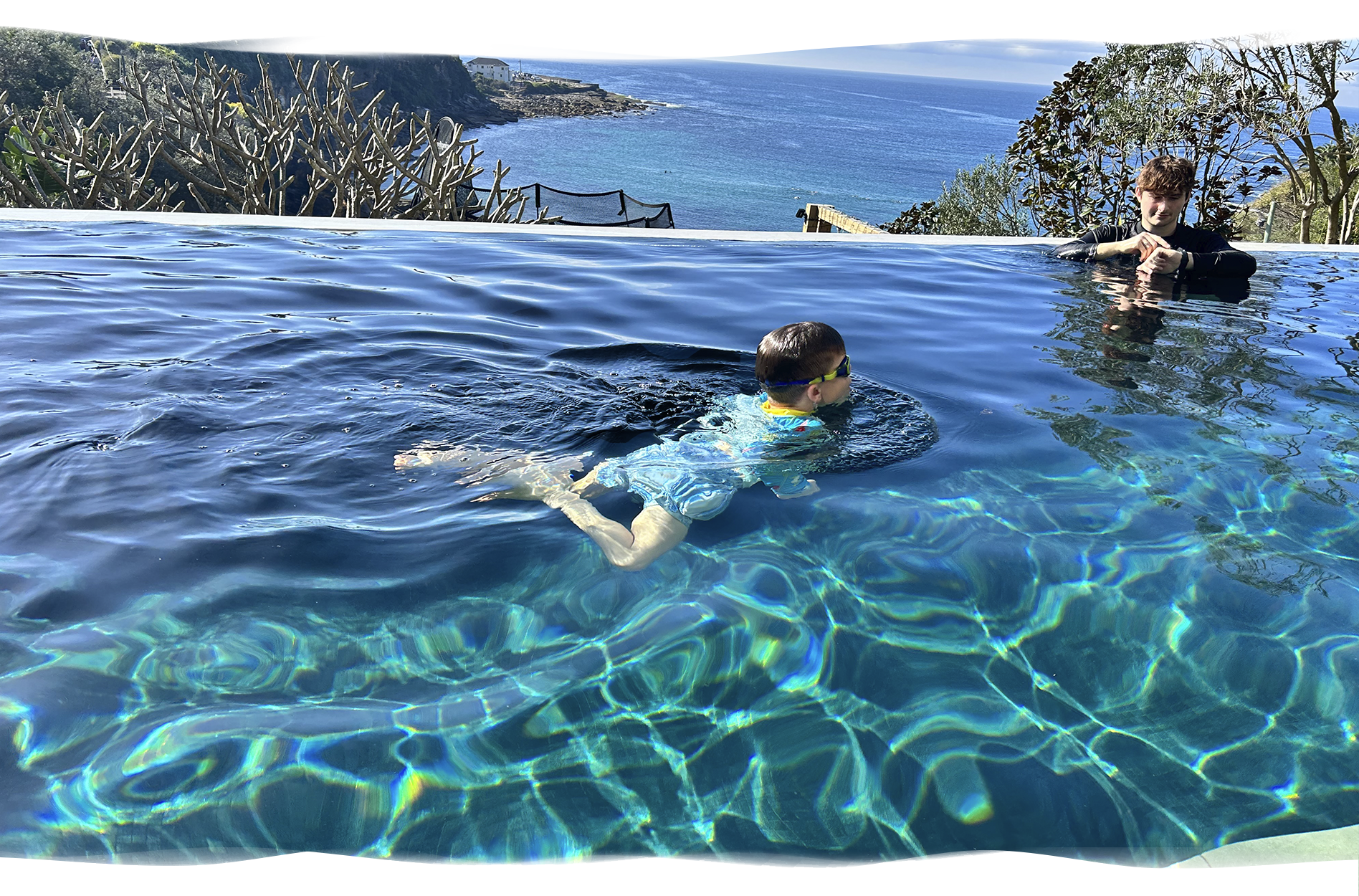 School-age boy prepares to dive through a floating hoop held by her Nereids swim teacher, highlighting confidence, focus, and playful stroke development.
